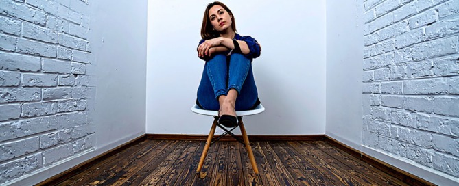 Frau sitzt mit verschränkten Armen in einem engen Raum und wirkt blockiert – Symbolbild für Leber-Qi-Stagnation und hormonellen Stillstand